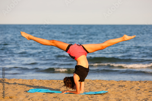 teenage girl with her head down does gymnastics by the sea
