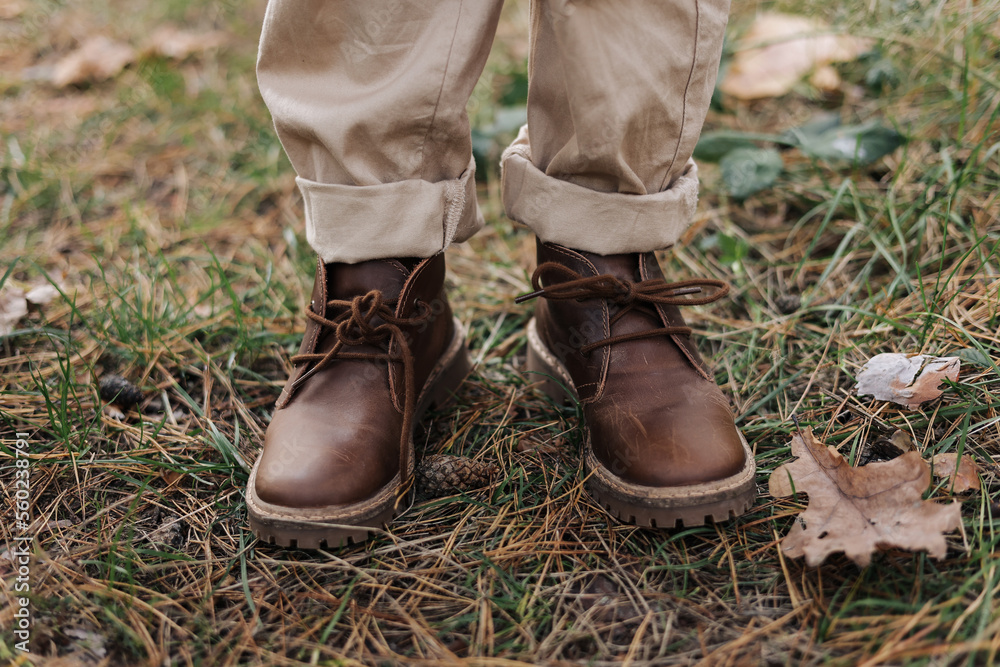 Cropped photo of kids legs in leather brown shoes and beige pants outdoors at autumn park with maple leaves Children adventure on fresh air. International Children's day