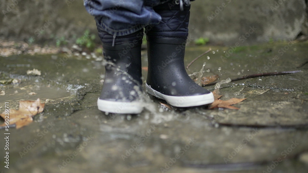 Child jumping into water puddle. Toddler wearing boots splash into puddle Child jumping into water puddle. Toddler wearing boots splash into puddle