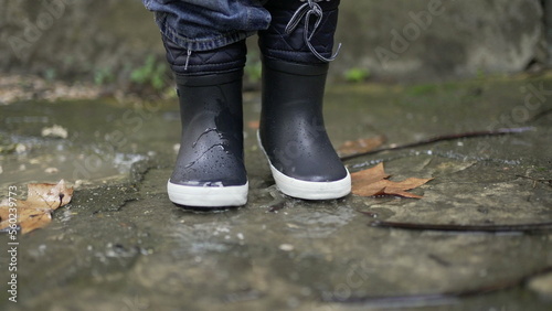 Child jumping into water puddle. Toddler wearing boots splash into puddle