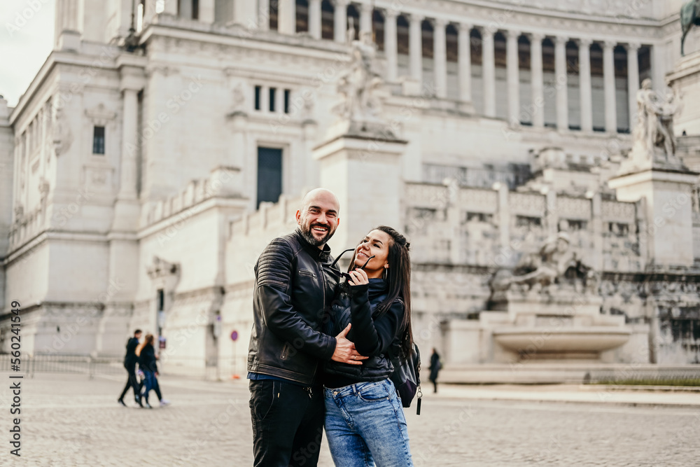 Happy  Tourists  couple traveling at Rome, Italy, poses in front of Altar of the Fatherland (Altare della Patria) and Piazza Venezia at, Rome, Italy