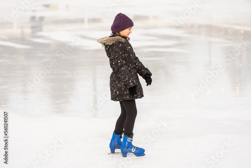 Adorable little girl in winter clothes skating on ice rink