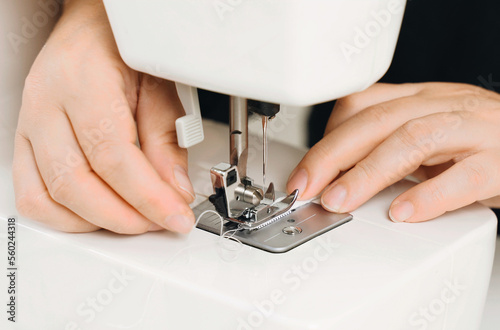 A female seamstress sews white fabric items on a sewing machine.