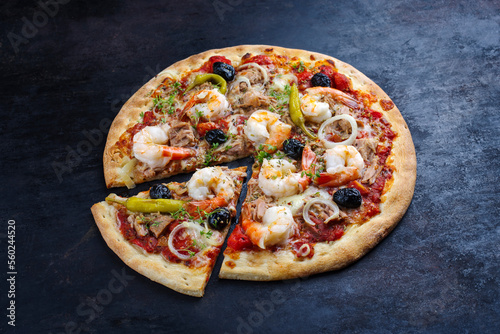 Traditionelle italienische Pizza frutti di mare Riesengarnelen, Tunfisch und Oliven serviert als close-up auf einem rustikalen schwarzen Board 