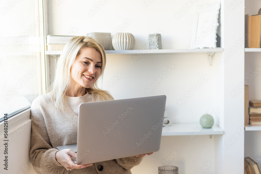 Beautiful young woman in casual clothing using laptop and smiling while working indoors Beautiful young woman in casual clothing using laptop and smiling while working indoors