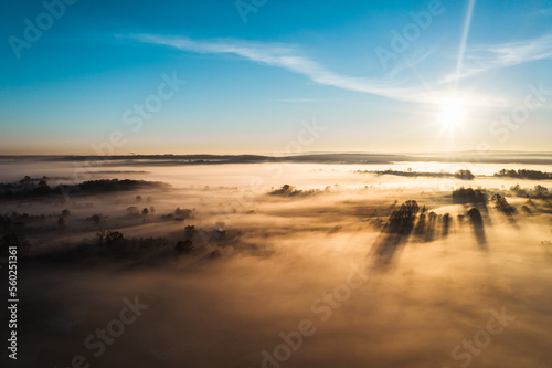 Flying over a village at dawn  bright sun on the horizon and fog over a small village.