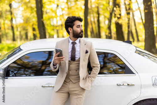 Business is his life. Handsome young arab businessman using smart phone while standing near his car outdoors © dianagrytsku