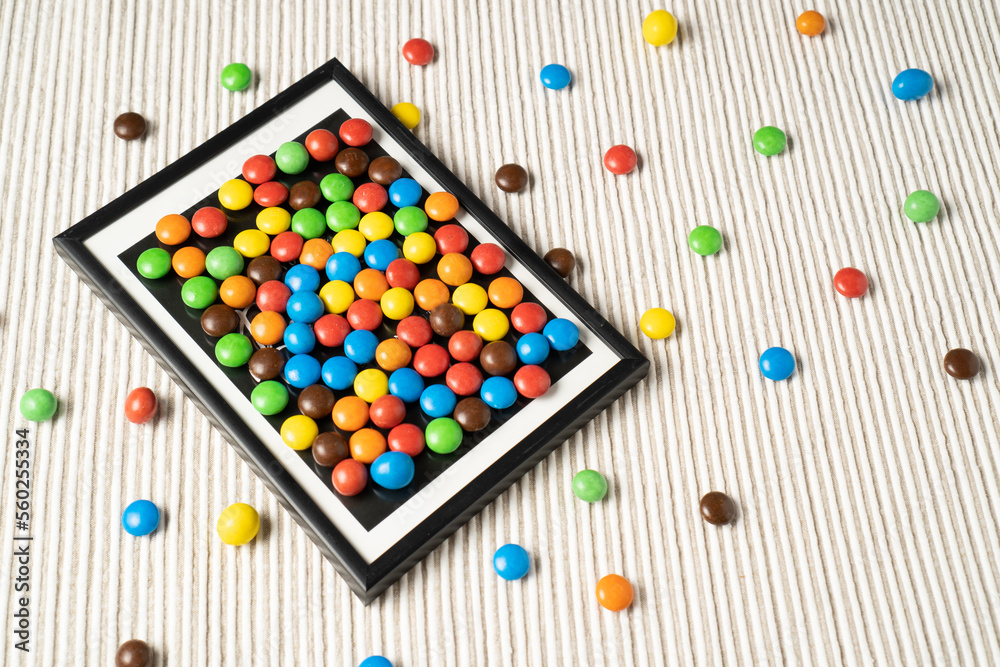 A playful and fun design with small dragee candies arranged like a picture in a frame on a white table. A playful and fun design with small dragee candies arranged like a picture in a frame on a white table.