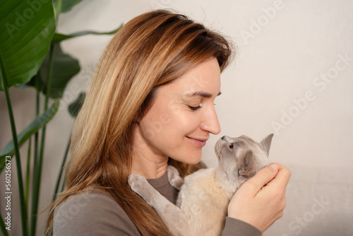 Portrait of young woman holding cute Burmese cat with yellow eyes. Female hugging her cute short hair kitty. Love between owner and cat.