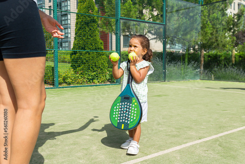 Little girl handing tennis balls to her mother on a padel tennis court