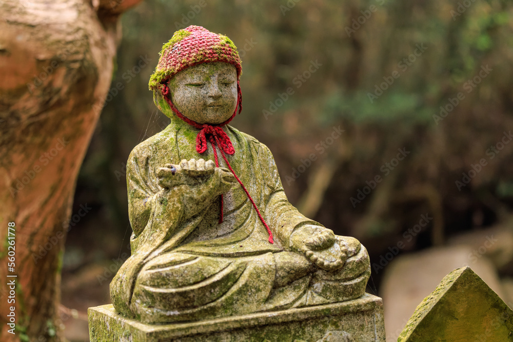 Stone statue of child sitting cross-legged wearing a knit cap at Japanese shrine Stone statue of child sitting cross-legged wearing a knit cap at Japanese shrine