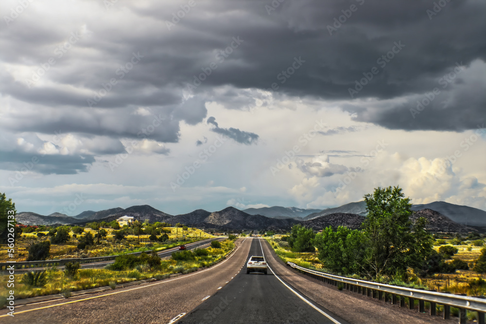 road trip through New Mexico USA - SUV travels on blacktop road toward distant mountains Dramatic sky - Saturated color - Room for copy