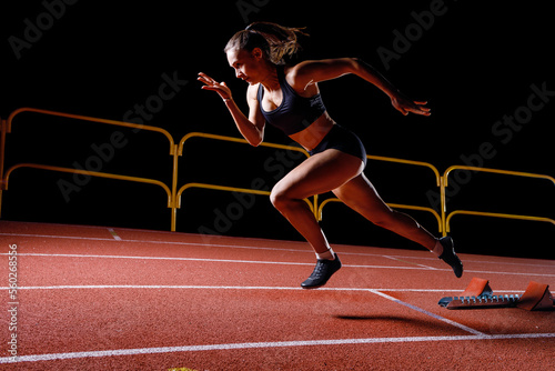 Young sportswoman doing explosive start from the starting blocks on her running lane.