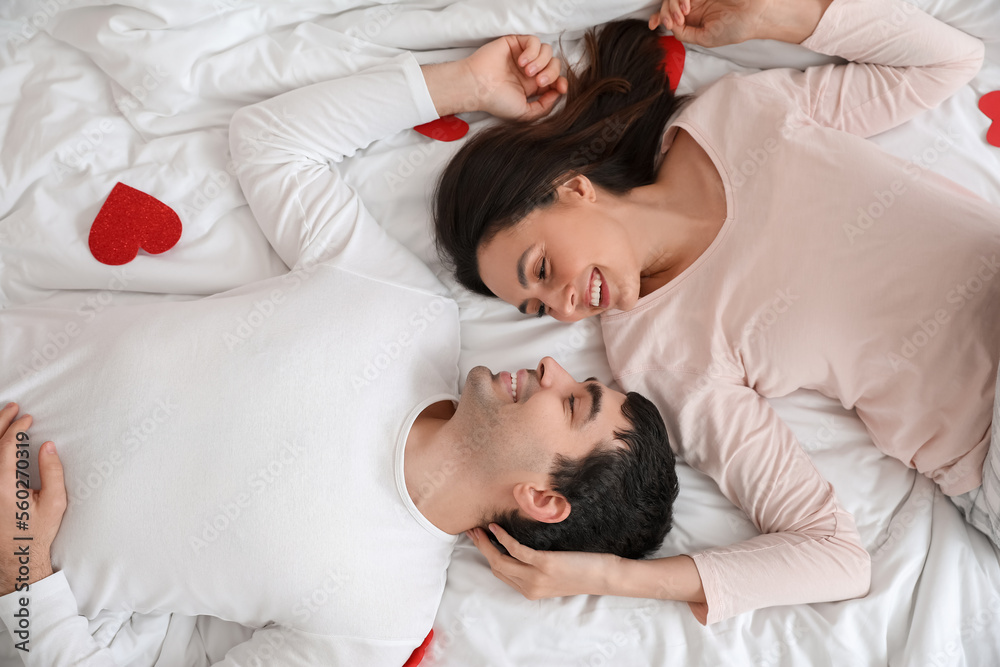 Young couple with paper hearts lying on bed. Valentine's Day celebration Young couple with paper hearts lying on bed. Valentine's Day celebration
