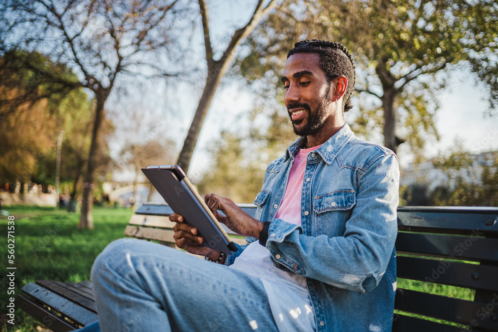 Young man sitting on a park bench using his digital tablet to check social media Young man sitting on a park bench using his digital tablet to check social media