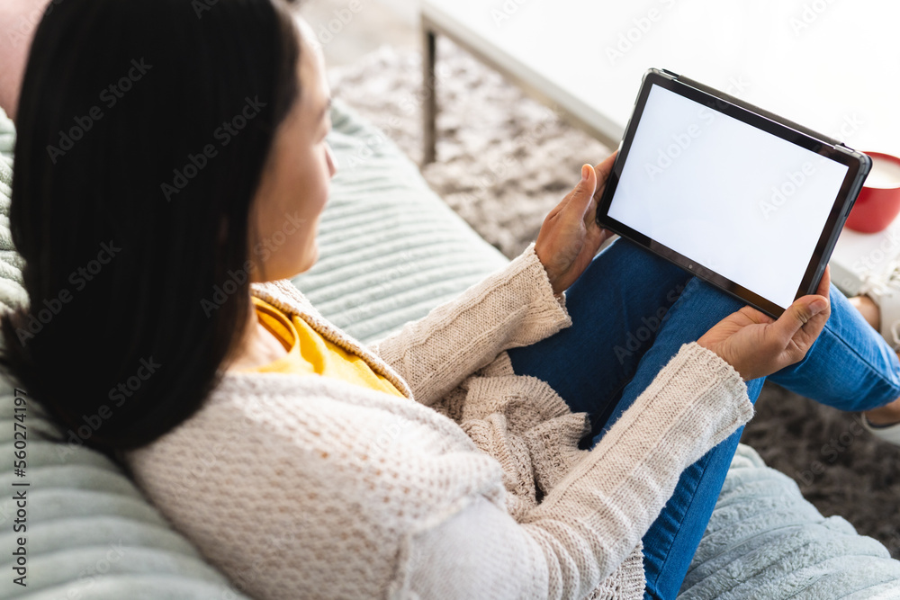 Asian woman sitting on sofa in living room and using tablet with copy space Asian woman sitting on sofa in living room and using tablet with copy space