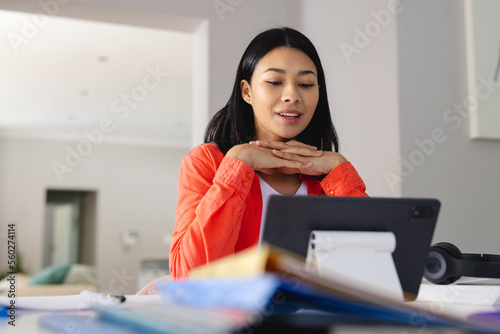 Image of biracial woman sitting at desk talking during video call on tablet at home, copy space