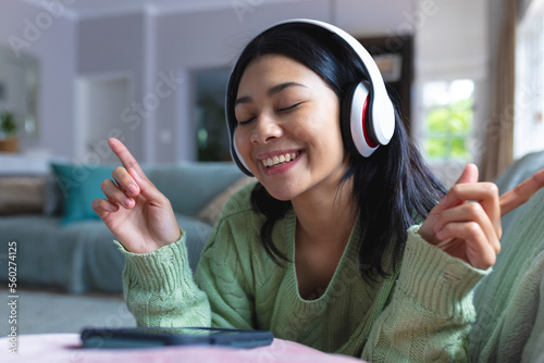 Image of happy biracial woman in headphones using smartphone relaxing on sofa at home, copy space