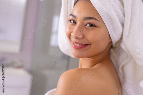 Portrait of happy biracial woman wearing towel smiling in bathroom, with copy space