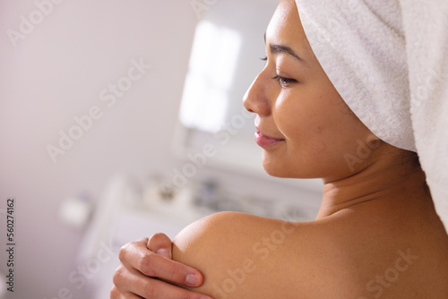 Happy biracial woman wearing towel smiling in bathroom, with copy space