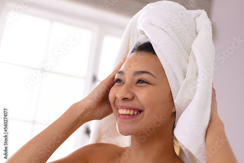 Happy biracial woman wearing towel on head smiling in bathroom, with copy space