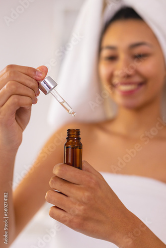 Vertical of smiling biracial woman in bathroom, holding essential oil dropper bottle, copy space