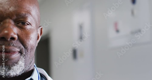 Video half face portrait of senior african american male doctor laughing in corridor, copy space photo