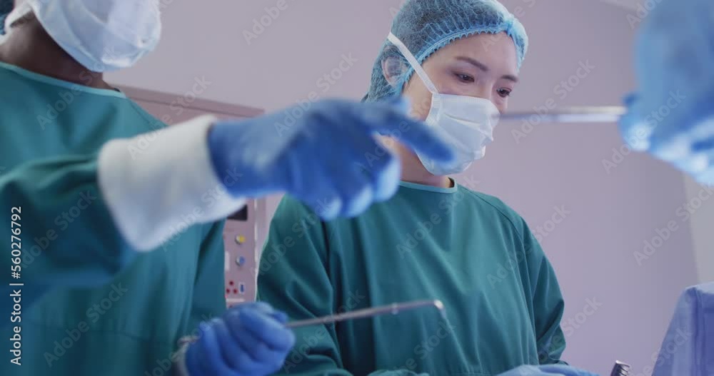 Video of asian female surgeon at work during operation in theatre and colleagues passing instruments