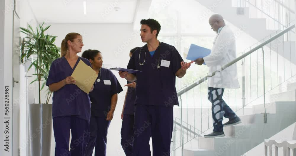 Video of diverse male and female doctors holding files talking as they walk in hospital corridor Video of diverse male and female doctors holding files talking as they walk in hospital corridor