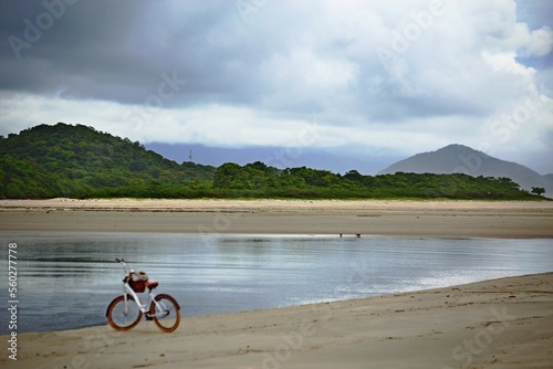 Bike standing on the sand of river side,, River with calm waters and green forest on the background. Itaguare beach, Bertioga, Brazil