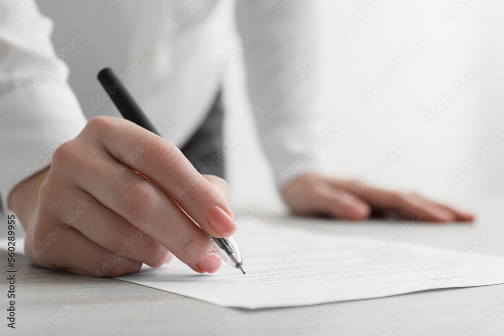 Woman signing documents at wooden table in office, closeup Woman signing documents at wooden table in office, closeup
