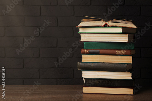 Stack of old hardcover books on wooden table near brick wall, space for text
