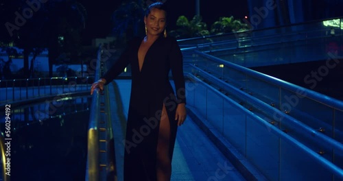 Sexy hispanic woman spins in the walkway of a glass building wearing a black dress at night photo