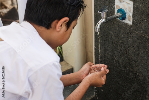 Back view of kid collect water on palm hands before cleansing face, ablution procedure before praying salah. 