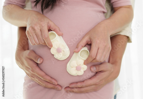 pregnant couple holding with hands together newborn baby shoes on belly