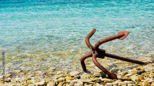 Closeup of an old grapnel anchor lying abandoned and rusting, on the water's edge of a pebbled beach in the Falkland Islands.