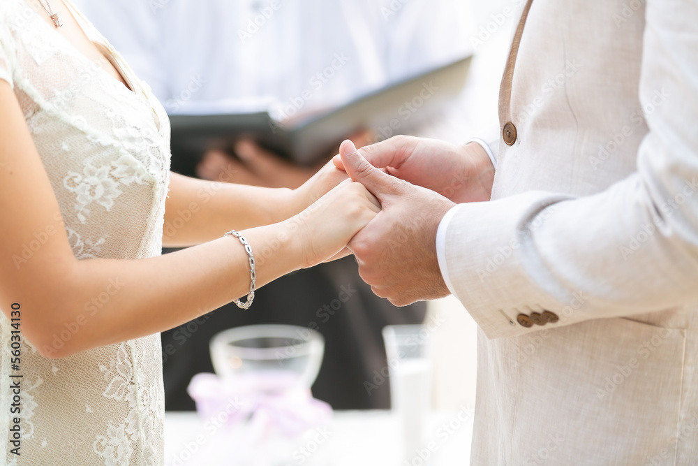 Fototapeta premium The couple, the groom and the bride, wear dresses, suits, she has a beautiful silver bracelet. holding hands together at wedding ceremony There was a pastor standing nearby as a witness.