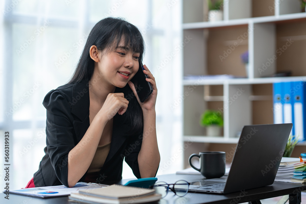 Obraz premium Business freelance asian woman talking on phone and working on laptop computer managing her business in workplace, doing business plan on calculator accounting financial report.