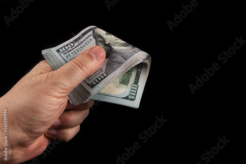 A man's hand holds a stack of banknotes in denominations of 100 American dollars on a black background
