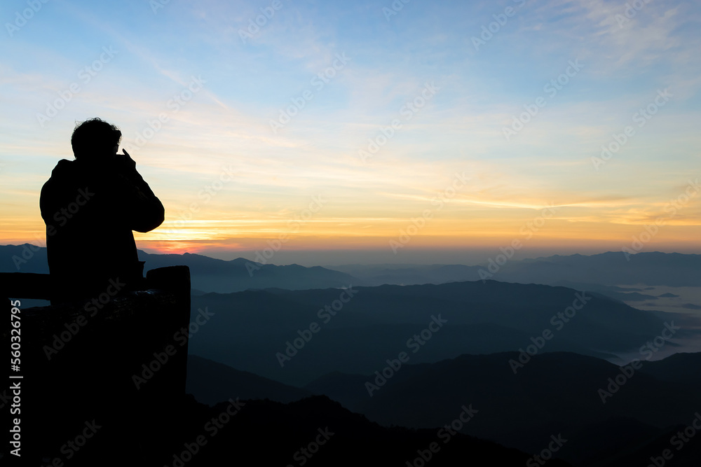 Silhouette of male photographer or traveler taking a photograph sunrise landscape on mountain.