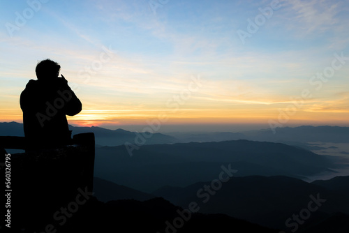 Silhouette of male photographer or traveler taking a photograph sunrise landscape on mountain.