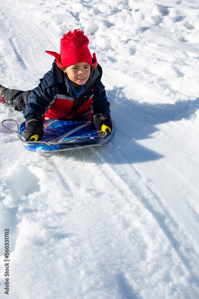 Cute African American boy sledding down the hill on a snowy day. Winter fun in the snow. Diverse child on a sled. Lots of copy space Cute African American boy sledding down the hill on a snowy day. Winter fun in the snow. Diverse child on a sled. Lots of copy space