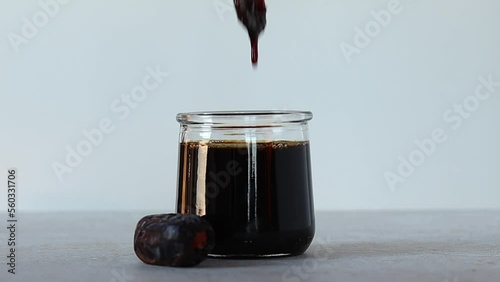 Date syrup dripping down a golden spoon. Eco sweetener in a glass jar nearly whole date fruit