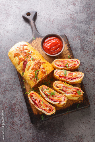 Freshly baked hot pizza stromboli roll with sausage and cheese close-up on a wooden board on the table. Vertical top view from above