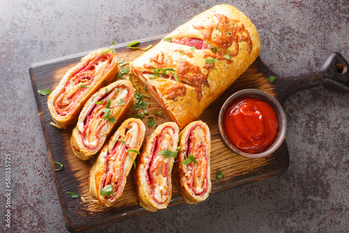Delicious pizza stromboli roll stuffed with salami sausage and mozzarella cheese close-up on a wooden board on the table. horizontal top view from above photo