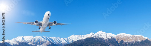 Large passenger jet airliner takes off rapidly over a mountain range against the background with a clear sky, banner wide view.