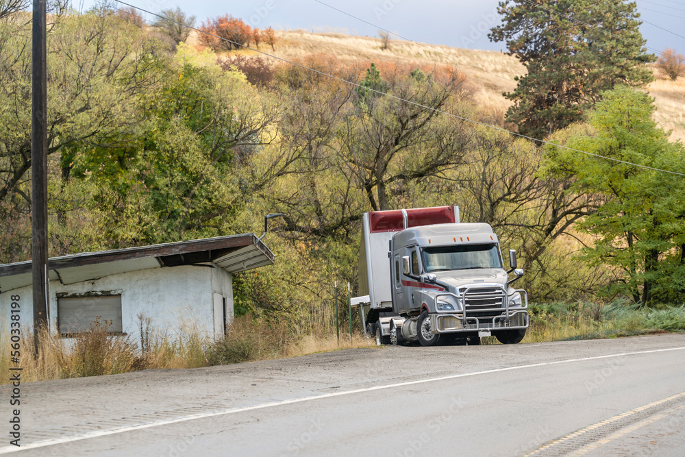 Gray big rig semi truck with dry van semi trailer standing on the driveway to the house on the side of the highway waiting for the next commercial flight