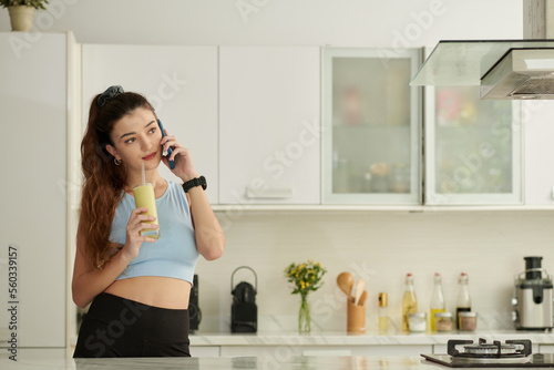 Portrait of young woman drinking fruit smoothie and talking on phone in the morning