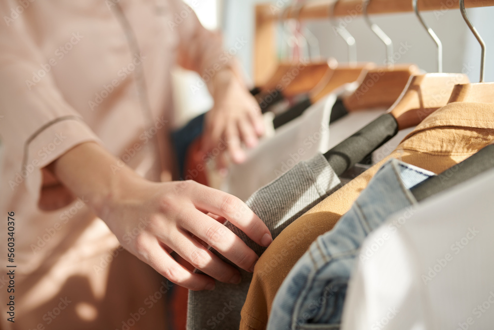 Close-up image of young woman in pajamas checking clothes on racks when choosing what to wear Close-up image of young woman in pajamas checking clothes on racks when choosing what to wear
