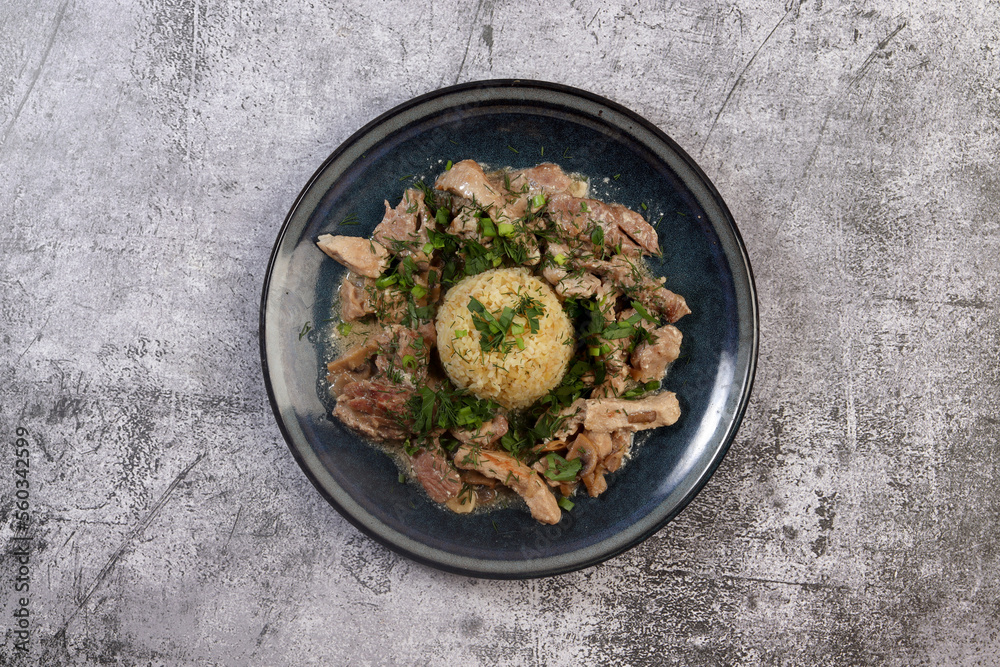 Pork stew with mushrooms and bulgur on a round plate on a dark background. Top view, flat lay Pork stew with mushrooms and bulgur on a round plate on a dark background. Top view, flat lay